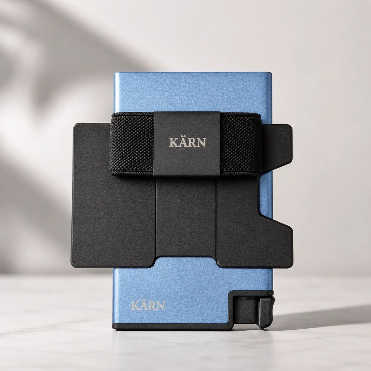 Tarjetero RFID KÄRN de aluminio azul con tarjeta visible, banda elástica negra y diseño slim para uso diario.