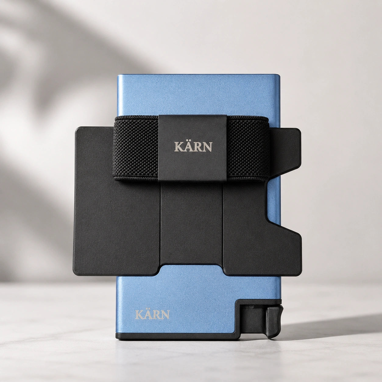 Tarjetero RFID KÄRN de aluminio azul con tarjeta visible, banda elástica negra y diseño slim para uso diario.