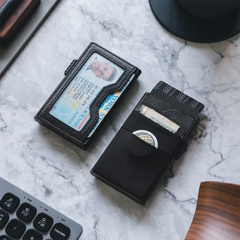 Tarjetero RFID KÄRN de piel negra sobre escritorio de mármol, con compartimento para monedas, tarjetas y billetes, diseño elegante y seguro.