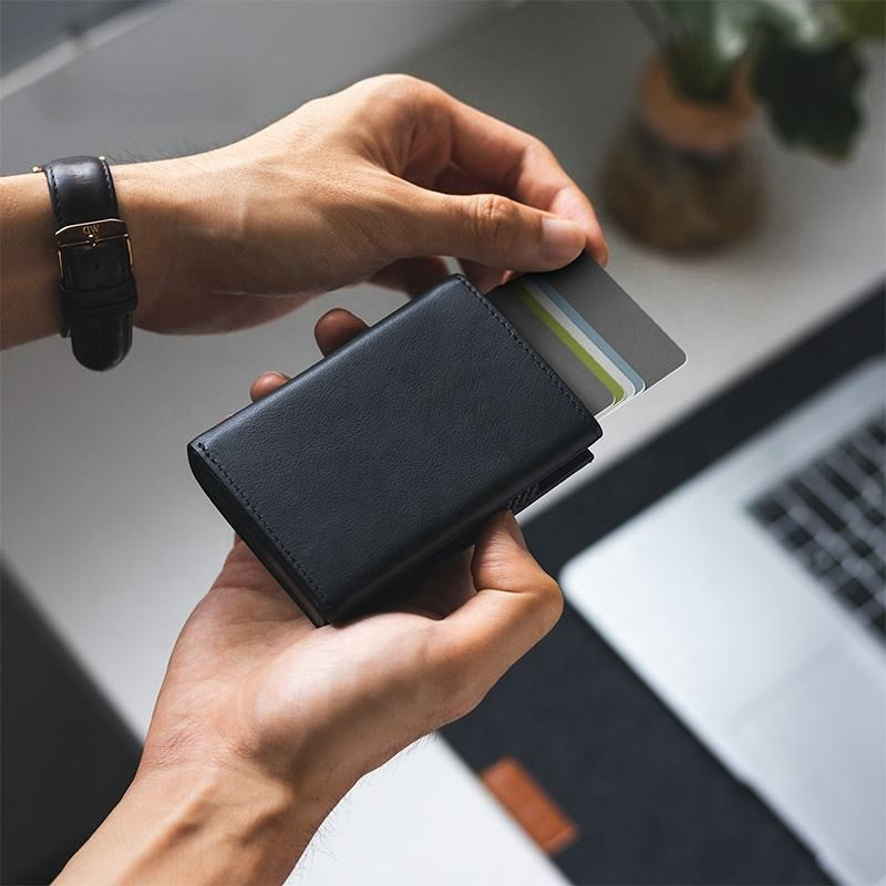 Manos usando tarjetero slim negro con acceso rápido a tarjetas y protección RFID sobre escritorio premium.